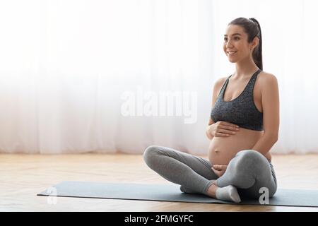 Junge, erwartete Frau, die zu Hause auf der Matte trainiert und sich auf die Geburt vorbereitet Stockfoto