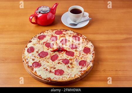 italienische Pepperoni-Pizza mit rotem Pfeffer auf einem Holzständer Mit Tee und Wasserkocher Stockfoto