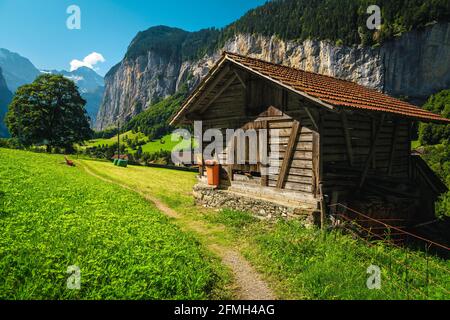 Typische alpine Holzscheune auf der grünen Weide und hohen Klippen im Hintergrund, Lauterbrunnental, Berner Oberland, Schweiz, Europa Stockfoto