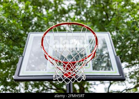 Nahaufnahme, die unter dem roten Basketballkorb mit Netz und aufschaut Glastafel auf dem Spielplatz mit Blick auf Himmel und Haus Im Hintergrund Stockfoto