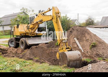 Ein Hydraulikkolben und ein Schaufelbagger graben den Boden Neben einem Sandhaufen auf einem Industriegelände Stockfoto