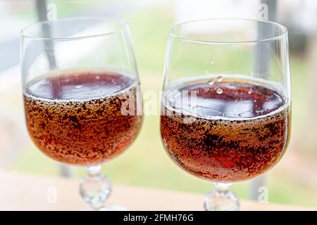 Seitenansicht von Cola-Limonade oder traditionellem russischen Kvass gegoren Brotgetränk in zwei Gläsern auf dem Tisch zu Hause vorbei Fenster mit kohlensäurehaltigen Blasen Stockfoto