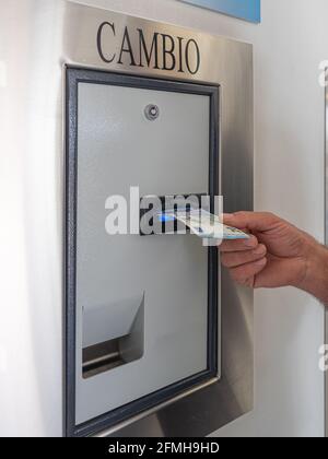 Man's Hand, der eine 20 Euro-Rechnung in einen Wechselautomaten steckt. Tauschen Sie Geldscheine gegen Münzen aus. Stockfoto