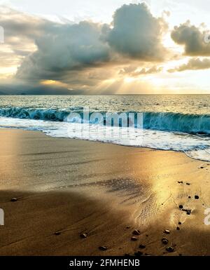 Sonnenstrahlen Brechen Durch Die Wolken, Wenn Die Sonne Untergeht Am Meereshorizont im vertikalen Bildformat Stockfoto