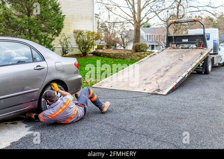 Herndon, USA - 21. November 2020: Auto in der Auffahrt mit Turmmann, der Kette am Abschleppfahrzeug anhängt, weil Kraftstoff ausläuft, der den mit Katze bedeckten Straßenbelag beschädigt hat Stockfoto