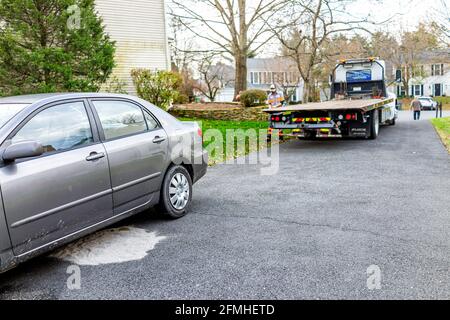 Herndon, USA - 21. November 2020: Geparktes Auto in der Auffahrt, wobei der Turmmann zum Abschleppen des Fahrzeugs läuft, da Kraftstoffleck den Straßenbelag beschädigt hat, der mit Kat. l Stockfoto