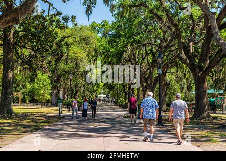 Savannah, USA - 11. Mai 2018: Berühmter Platz mit Wasserbrunnen im Forsyth Park in Georgia während eines sonnigen Tages im Sommer mit Leuten, die auf einer Gasse spazieren gehen Stockfoto