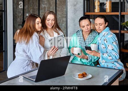 Beim Frühstück sehen sich eine Gruppe von Frauen Nachrichten und Nachrichten auf mobilen Geräten an und sitzen am Tisch im Speisesaal. Stockfoto