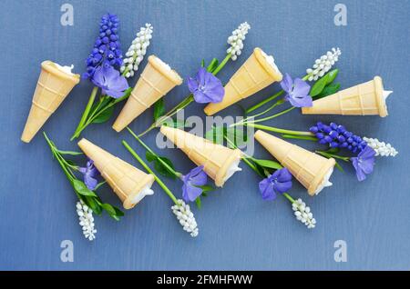 Köstliches Dessert in Waffelkegel auf blauem Hintergrund mit Frühlingsblumen. Draufsicht Stockfoto