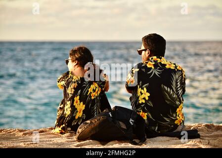 Ehepaar, das den Sonnenuntergang beobachtet, trägt passende Hawaiihemden mit Blumendrucken, Sunset Beach, Haleiwa, Hawaii, USA Stockfoto