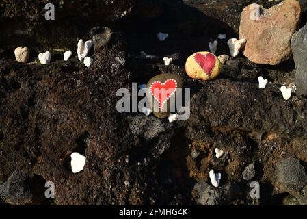 Herzförmige Korallen und Steine, bemalt mit leuchtend roten "Liebesherzen", in vulkanischen Felsen am Ufer des Sandy Beach Park, Oahu, Hawaii, USA platziert Stockfoto