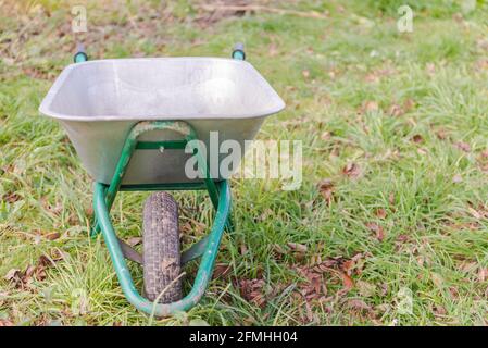 Schubkarre für die Arbeit im Land. Im dicken Gras sitzt eine Aluminium-Schubkarre für den Garten. Stockfoto