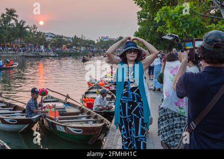 Tourist posiert mit den Händen über dem Kopf und die Sonne geht hinter ihr unter als Partner fotografiert, Hoi an, Vietnam Stockfoto