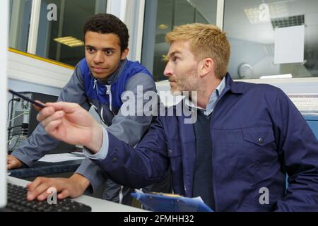 Junger Lehrling, der etwas im Computer überprüft Stockfoto