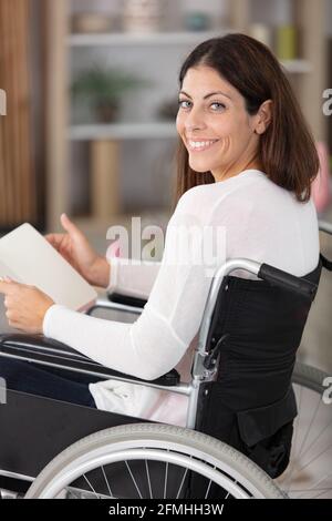 Schöne junge behinderte Frau im Rollstuhl, die ein Buch liest Stockfoto