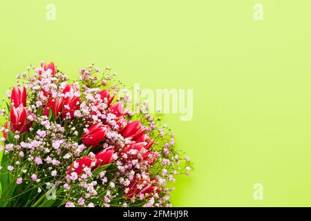 Rote Tulpen und Gypsophila Blumen Bouquet auf grünem Hintergrund, selektiver Fokus. Muttertag, Geburtstagsfeier Konzept. Draufsicht, Kopierbereich für Stockfoto