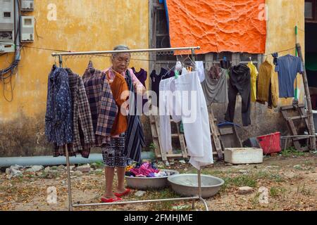 Ältere vietnamesische Dame, die vor dem Haus in Hoi an, Vietnam, Kleidung an der Wäscheleine aufgehängt hat Stockfoto