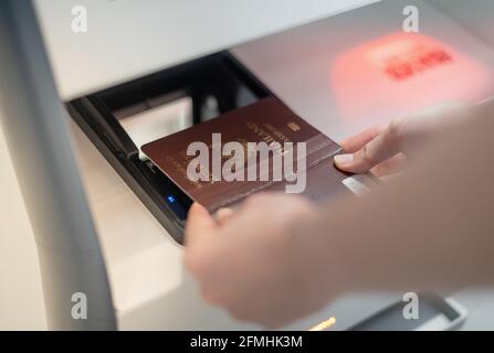 Weibliche Hand mit persönlichem Reisepass, der am Check-in-Schalter gescannt wird, um die Bordkarte am Flughafenterminal zu erhalten. Stockfoto