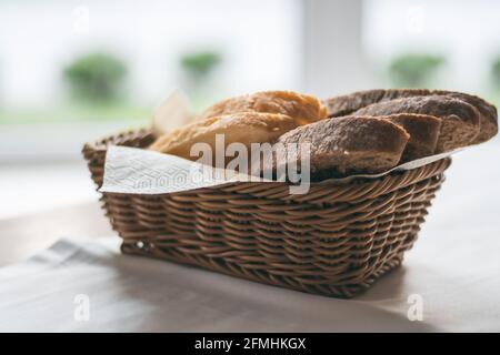 Korbkorb mit schwarzem und weißem Brot auf weißer Tischdecke In der Nähe des Fensters Stockfoto