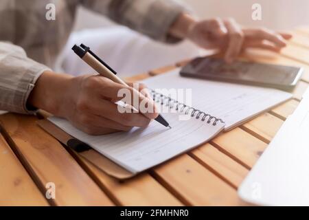 Nahaufnahme junge Geschäftsfrau Hände mit Stift Schreiben Notizen auf Papier. Weibliche Führungskraft sitzt am Tisch im Home Office. Die Hände der Frau schreiben spiralförmig Stockfoto