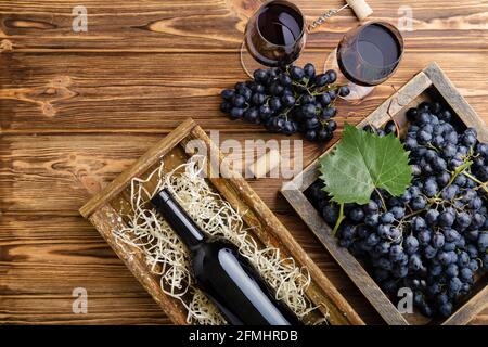 Komposition aus Rotwein auf braunem Holztisch. Draufsicht. Rotwein Flasche Korkenzieher Korken Weingläser schwarze reife Trauben in Box auf Holztisch. Flach liegend Stockfoto