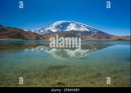 Muztagata Berg spiegelt sich in den Gewässern der Karakul See am Karakorum Highway, Provinz Xinjiang, China Stockfoto