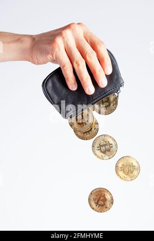 Isoliertes Bild einer kaukasischen Frau, die eine schwarze Handtasche vor hellweißem Hintergrund hält. Bitcoin-Münzen fallen vom Geldbeutel, als sie leert. Weinen Stockfoto