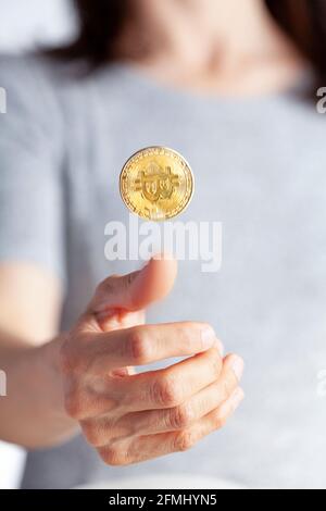 Eine Frau dreht eine Münze mit einem hellen Bitcoin. Ein Konzept für Investitionen in Kryptowährung und deren riskanter Ungewissheit. Es kann gehen Stockfoto