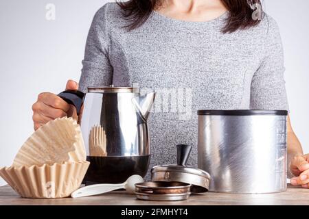 Eine junge kaukasische Frau bereitet Kaffee auf dem Tisch mit einem Perkolator-Filterpapier und einem Glas Kaffee zu. Sie ist vor weißem Hintergrund. Hausgemachte m Stockfoto