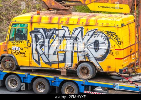 Sehr alter gelber Mercedes Benz Sprinter Van; Graffiti, Rattenlook, bemalte Grafiken, Straßenkunst und individuelle Grafiken auf altem Vintage-Van, klassische Autos. Ein heruntergekommenes, verfallenes Restaurierungsprojekt, 50s Scheunensuche nach dem Krieg. Rostige, verkrustete, gebrochene, markierte korrodierte Fahrzeuge, verrosteter Schrott-LCV auf einem Anhänger, der in der Nähe von Manchester, Großbritannien, fährt Stockfoto