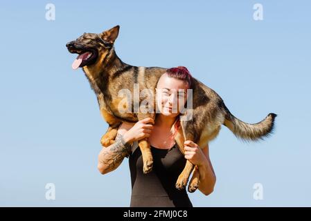 Tätowierte weibliche Athletin mit niedlichen reinrassigen Hund auf den Schultern suchen An sonnigen Tagen vor der Kamera Stockfoto
