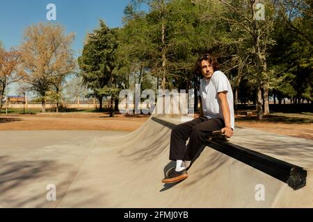 Junger Mann, der auf dem Skateboard sitzt, um sich auszuruhen Stockfoto