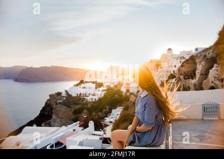 Rückansicht einer nicht erkennbaren weiblichen Reisenden, die Oia Village bewundern Santorini Insel an windigen Tagen in Griechenland Stockfoto