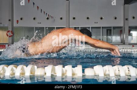 Seitenansicht eines starken männlichen Schwimmers in der Badekappe Schmetterlingsschlag während des Trainings im Swimmingpool mit blauem Wasser Stockfoto