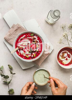 Draufsicht auf die Ernte unkenntlich Person Rühren Matcha Tee in tasse mit süßer, kalter Beerensuppe auf den Tisch gelegt Popsicle in der Schüssel Stockfoto