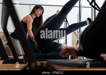 Flexible weibliche Stretching Beine mit Hilfe von persönlichen Lehrer während Übungen auf Pilates Reformer Stockfoto
