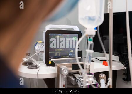 Seitenansicht der Ernte anonyme Tierärztin in Maske gegen Professionelles medizinisches Gerät mit Grafiken und Zahlen auf dem Bildschirm Stockfoto