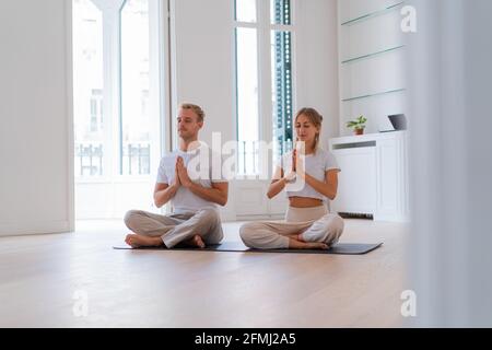 Friedliches Paar, das in Lotus-Pose mit Gebetshänden sitzt Gemeinsam Yoga praktizieren und mit geschlossenen Augen meditieren Stockfoto