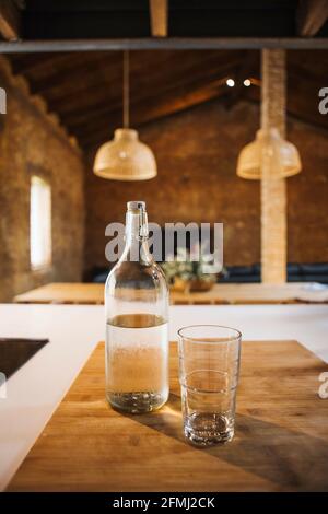 Transparente Flasche und Glas aus reinem Aqua auf Holzhacken Brett mit Schatten in der Hausküche Stockfoto