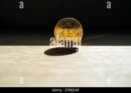 Metallmünze mit Ornament und Buchstaben, die das Kryptowährungssymbol auf darstellen Schreibtisch mit Schatten auf dunklem Hintergrund Stockfoto