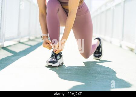 Crop junge kontemplative weibliche Athletin in Sportbekleidung binden Schnürsenkel auf Schuhe an sonnigen Tagen Stockfoto