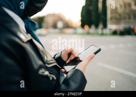 Seitenansicht der muslimischen Frau in Hijab und Schutzmaske Messaging in sozialen Medien auf dem Mobiltelefon während des Stehens City Street Stockfoto
