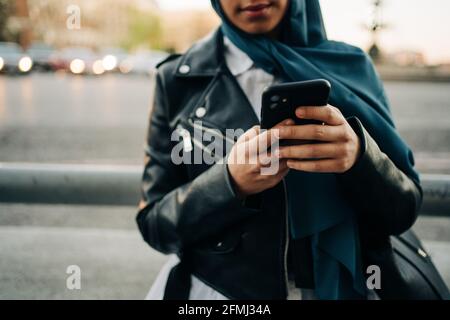 Crop muslimische Weibchen im Kopftuch stehen auf der Straße der Stadt und Durchsuchen des Mobiltelefons Stockfoto