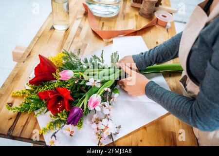 Von oben beschnitten unkenntlich weibliche Floristin in legerer Kleidung und Schürze arrangiert einen eleganten Blumenstrauß im Laden Stockfoto