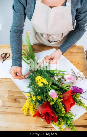 Von oben beschnitten unkenntlich weibliche Floristin in legerer Kleidung und Schürze arrangiert einen eleganten Blumenstrauß im Laden Stockfoto