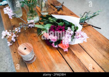 Hochwinkel elegant eingewickelt Bouquet mit frischen Rosen und sortiert Rosa Blumen geschnürt auf Holztisch neben Glas Vasen in Speichern Stockfoto