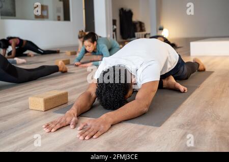 Gesellschaft von verschiedenen Menschen sitzen auf Matten in Kapotasana und Stretching Körper während des Yoga-Übens während des Unterrichts in geräumigen Studio Stockfoto