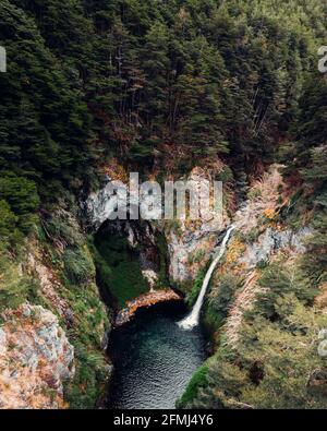 Spektakuläre Drohnenansicht des mächtigen Wasserfalls, der in den Fluss fließt see im Bergwald Stockfoto