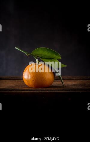 Ganze ungeschälte Mandarine mit Pediküre und welligen Blättern mit spitz Kanten auf Holzoberfläche Stockfoto