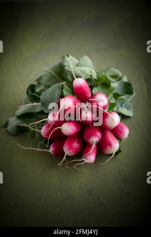 Haufen roher Rettich mit gebogenen Blättern und Wurzeln Grüner Hintergrund Stockfoto